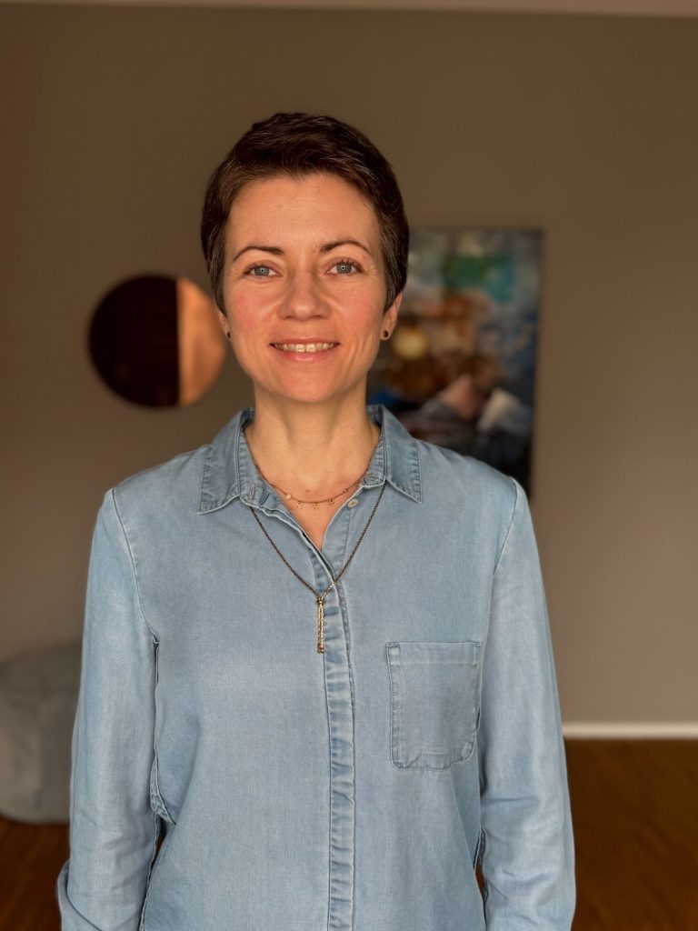 Janina Weingarth ist stehend neben einem Gemälde abgebildet. Janina bietet Paarberatung und Sexualberatung in Frankfurt.